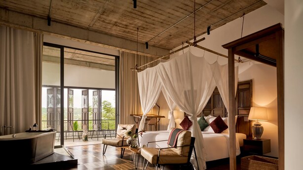A spacious bedroom with a large bed, a sitting area, a bathtub, and a view of the outdoors. - aNhill Boutique (Hue)