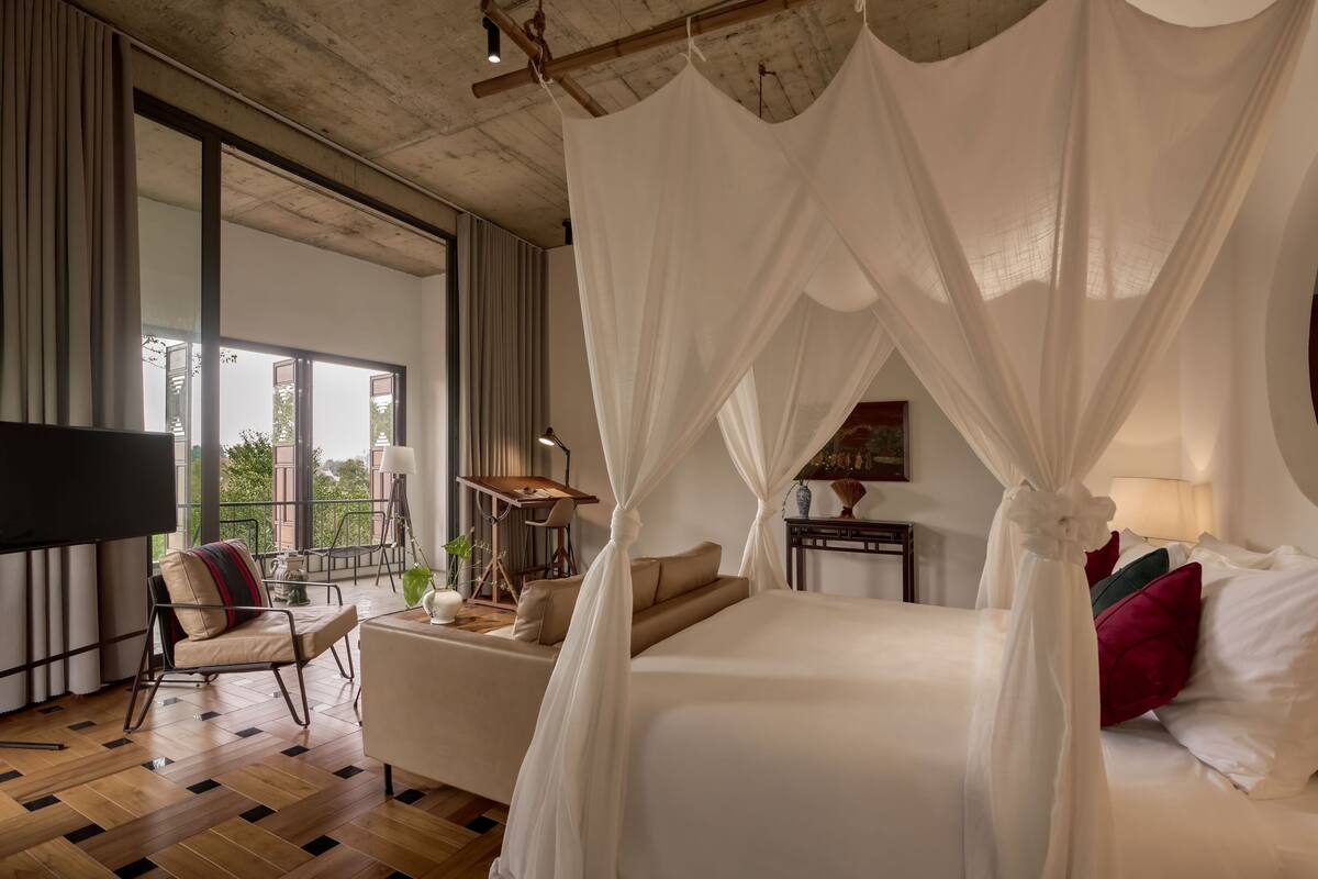 A bedroom with a large bed, a TV, a sofa, and a balcony with a view.