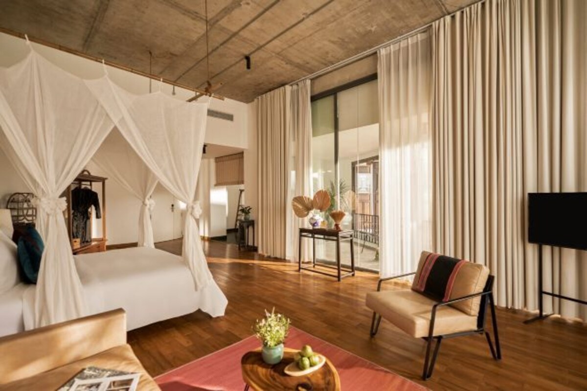 A spacious room with a large bed, a sitting area, and a balcony with curtains.