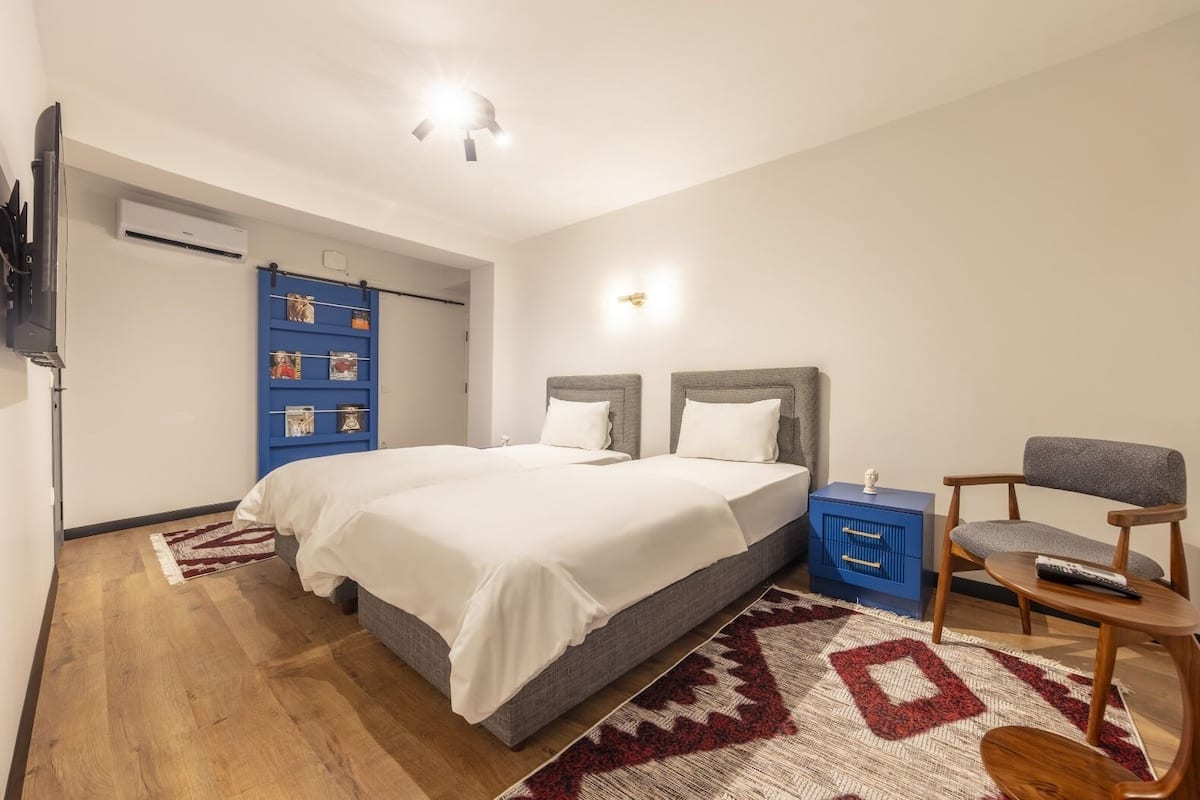 A modern bedroom with a large bed, a nightstand, a chair, and a blue shelving unit.
