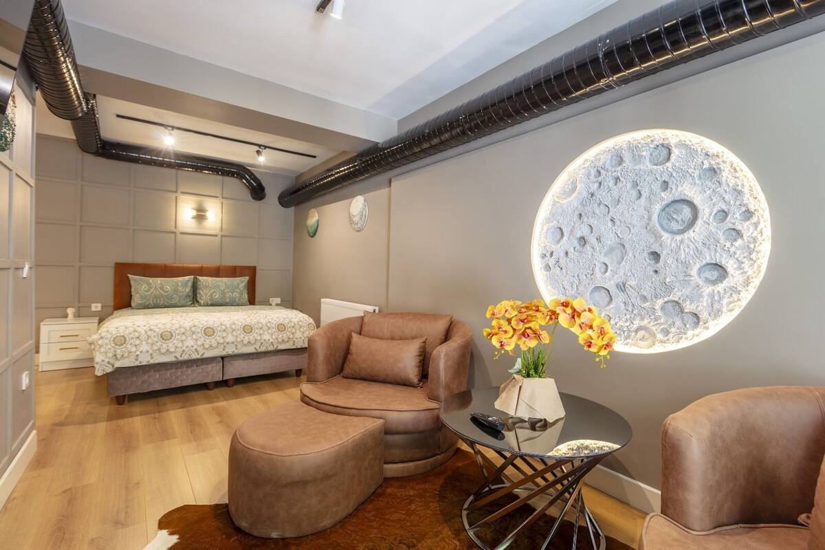 A modern bedroom with a bed, a sofa, a round table, and a unique moon-shaped light fixture.