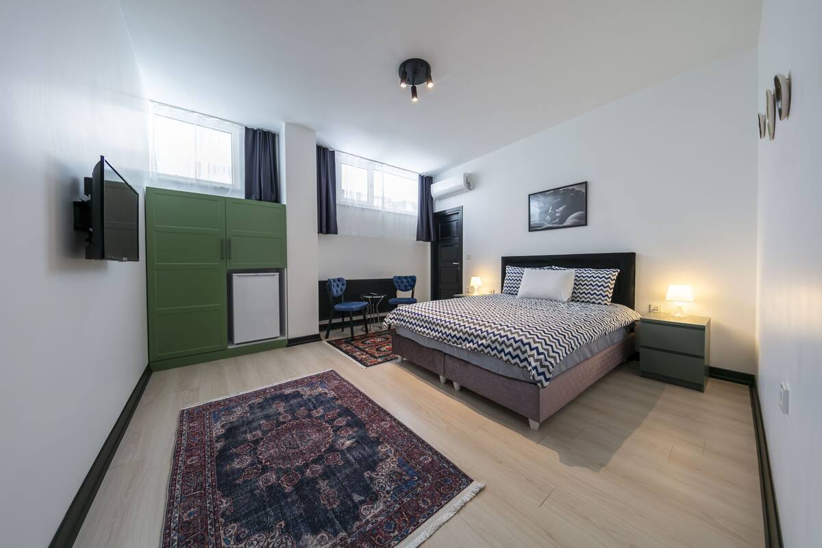 A modern bedroom with a large bed, a green wardrobe, a desk, and a TV.