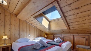 Une chambre confortable située sous les toits, avec deux lits, des murs en bois, une lucarne et un tapis à carreaux.