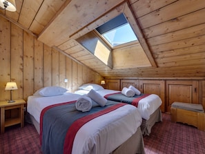 A cozy attic bedroom with two beds, wooden walls, a skylight, and a plaid carpet.