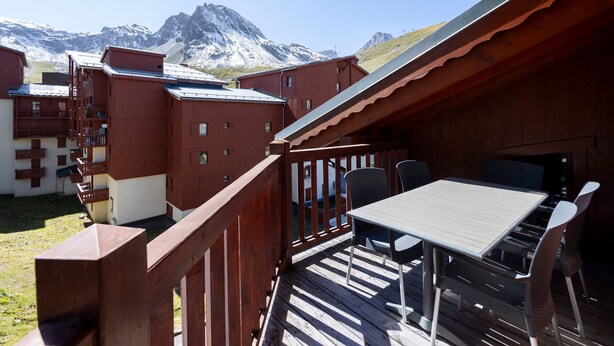 Une terrasse en bois avec une table et des chaises, offrant une vue sur un paysage montagneux.
