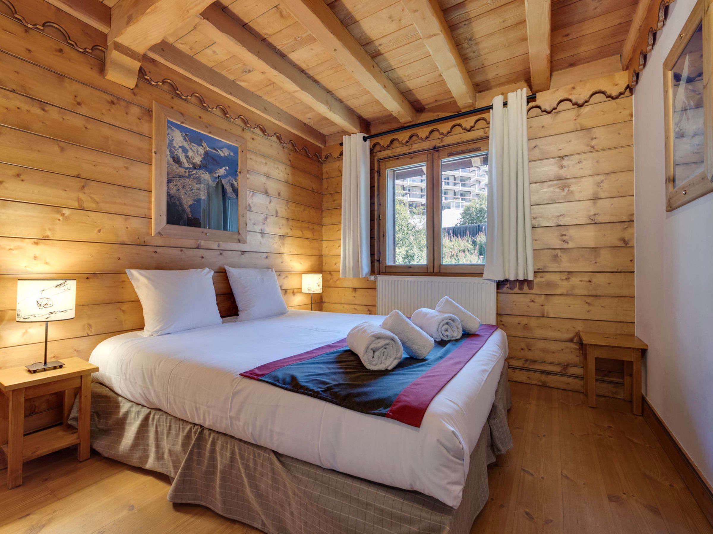 A wooden room with a bed, a window, and a painting on the wall.