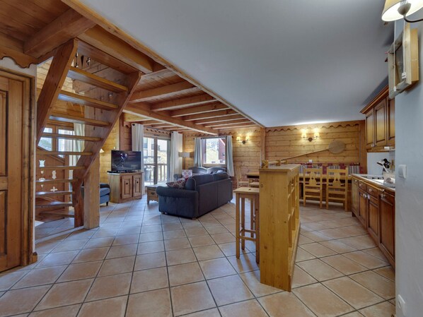 Amplia sala de estar con una escalera de madera, televisor, sofá y comedor con sillas y mesa de madera.
