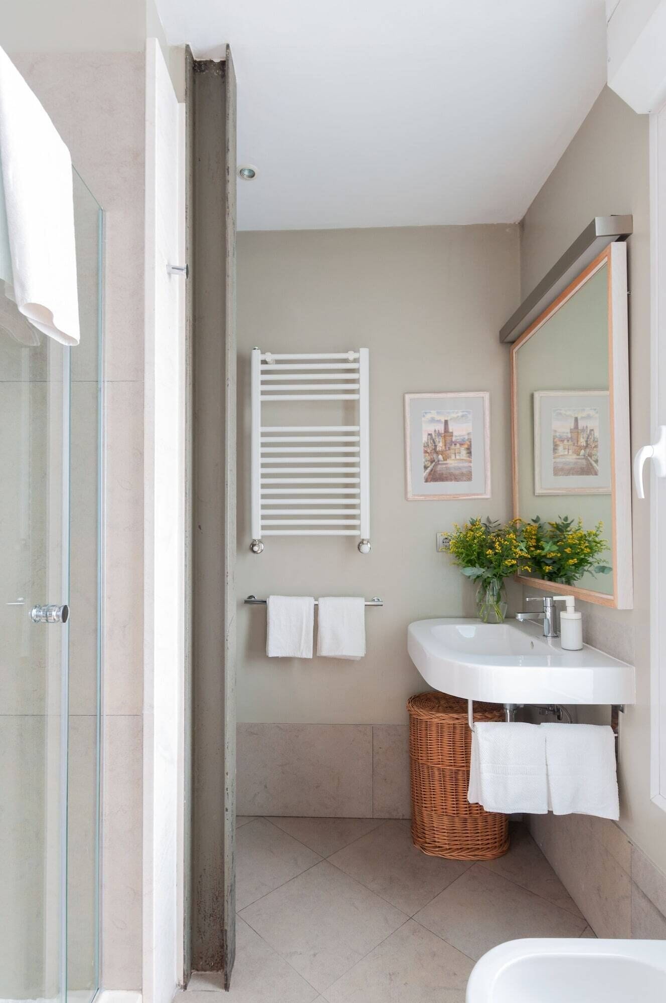 A modern bathroom with a glass shower enclosure, a white sink with a mirror above, and a wicker basket.