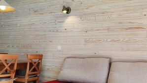 A room with a wooden wall, a red sofa, two grey cushions, a wooden table with chairs, and a hanging light fixture.