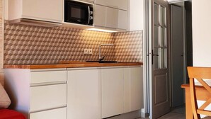 A compact kitchen with white cabinets, a microwave, and a patterned backsplash.