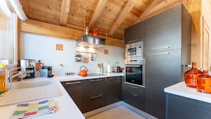 A modern kitchen with wooden ceiling beams, stainless steel appliances, and a white countertop. - Chalet Mountainside avec sauna et jacuzzi à 200m des pistes (Vars)