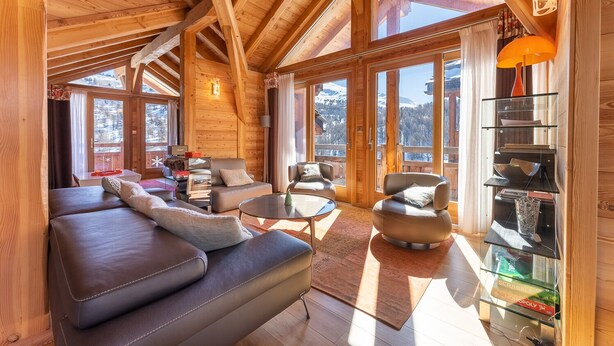 A spacious wooden interior with a high ceiling, large windows offering mountain views, a leather sofa, and a glass coffee table. - Chalet Mountainside avec sauna et jacuzzi à 200m des pistes (Vars)