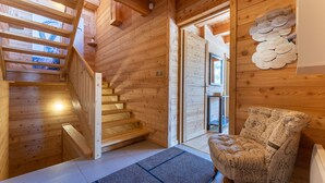 A wooden interior with a staircase, a chair, and a wall with circular wooden decorations. - Chalet Mountainside avec sauna et jacuzzi à 200m des pistes (Vars)