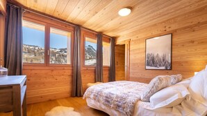 A cozy wooden room with a bed, a desk, and large windows offering a view of a snowy landscape. - Chalet Mountainside avec sauna et jacuzzi à 200m des pistes (Vars)