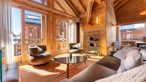 A spacious living area with wooden beams, large windows, and a cozy seating arrangement. - Chalet Mountainside avec sauna et jacuzzi à 200m des pistes (Vars)