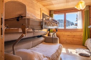 A cozy cabin with bunk beds, a window with a view of a snowy landscape, and a wooden interior.