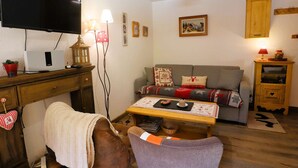 Ein gemütliches Wohnzimmer mit Fernseher, einem Holztisch, einer Couch, einem Tisch mit Unterlage und einer Lampe.