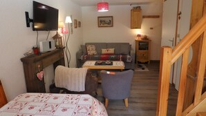 Ein gemütliches Zimmer mit Bett, einer Couch, einem kleinen Tisch, einem Fernseher und einer Holztreppe.