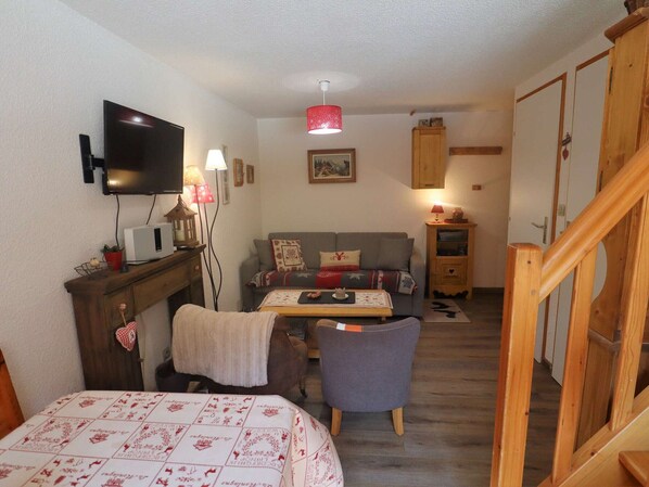 A cozy room with a bed, a sofa, a small table, a TV, and a wooden staircase.