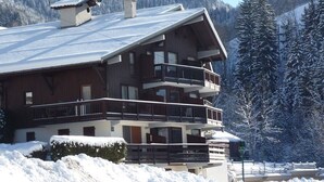 Ein mehrstöckiges Chalet mit Balkonen vor einer verschneiten Berglandschaft.
