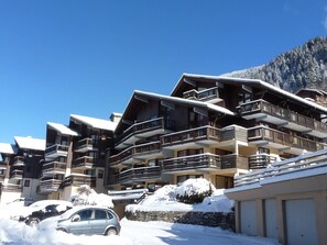 Un hôtel à plusieurs étages doté de balcons, entouré d’un paysage enneigé et ayant une chaîne de montagnes en toile de fond.