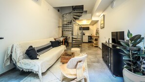 Un salon moderne avec un canapé, une chaise en bois, une table basse, un meuble noir et une plante en pot.