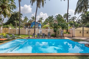 Una piscina amb gandules, palmeres i una casa al fons.