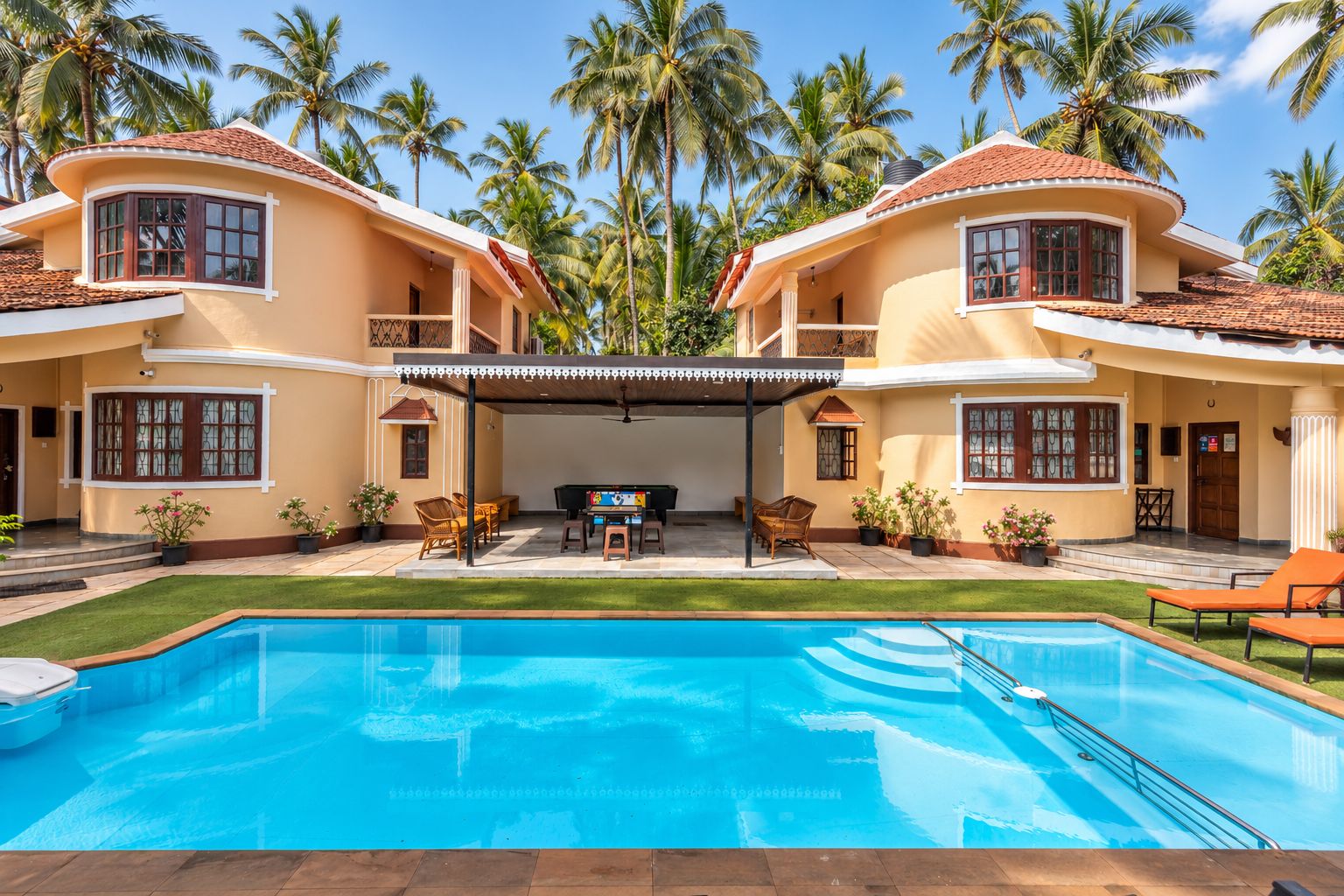 A two-story house with a swimming pool, outdoor seating, and palm trees.
