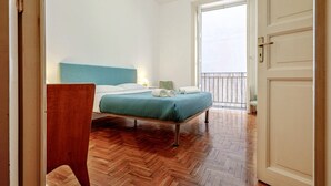 A bedroom with a bed, wooden floor, and a door leading to a balcony.