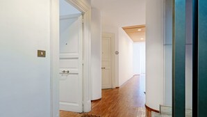 A hallway with wooden flooring, white walls, and a door leading to another room.
