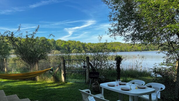 A table set outdoors with chairs, a hammock, and a view of a lake.