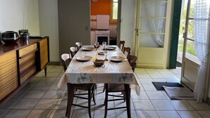 A dining area with a table set for four, chairs, a kitchen in the background, and a door leading outside.