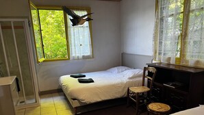 A bedroom with a bed, a chair, a desk, and a window with a decorative hanging.