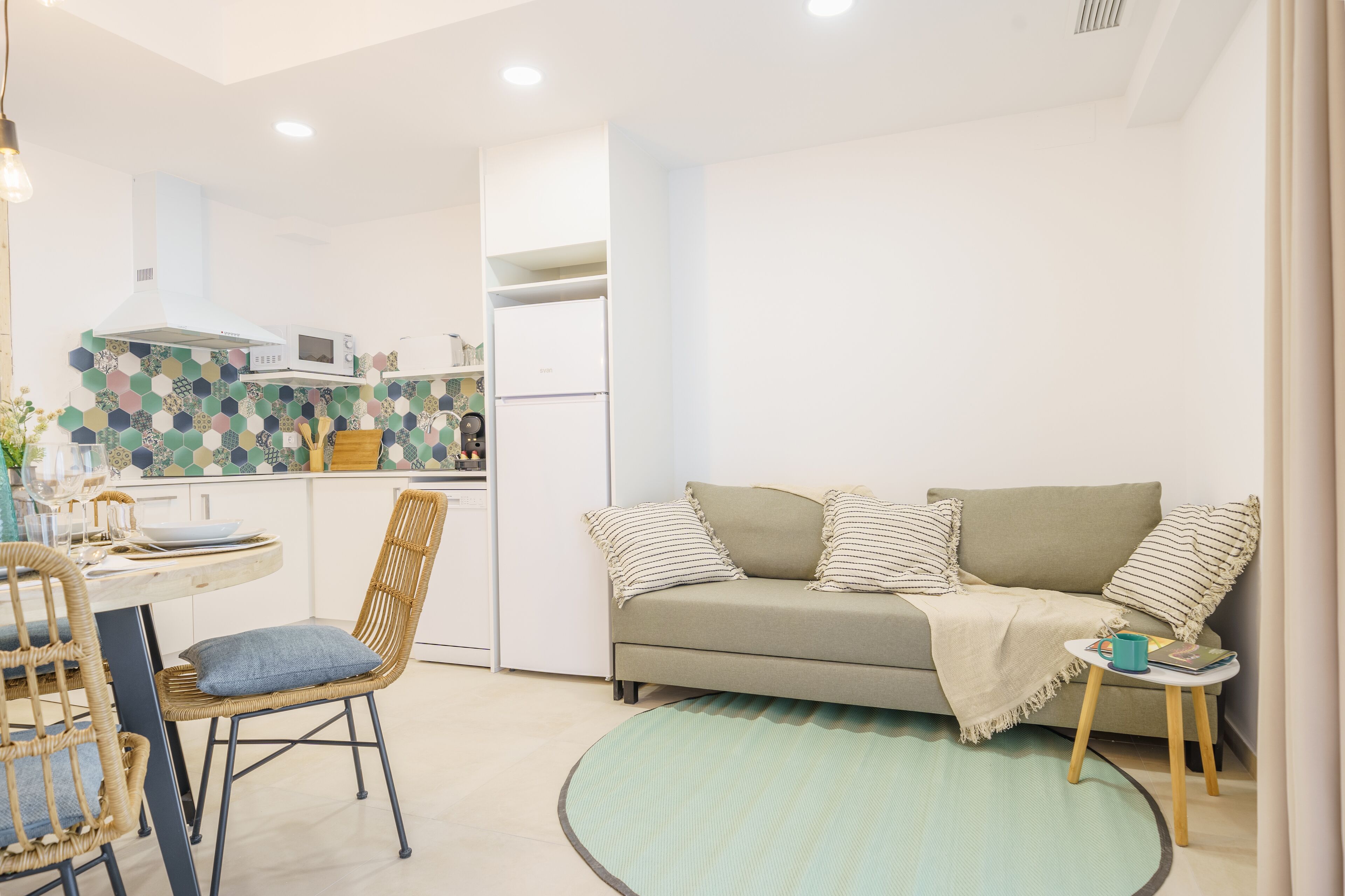 A compact living space with a kitchenette, a dining area with a table and chairs, and a sofa with a throw blanket.