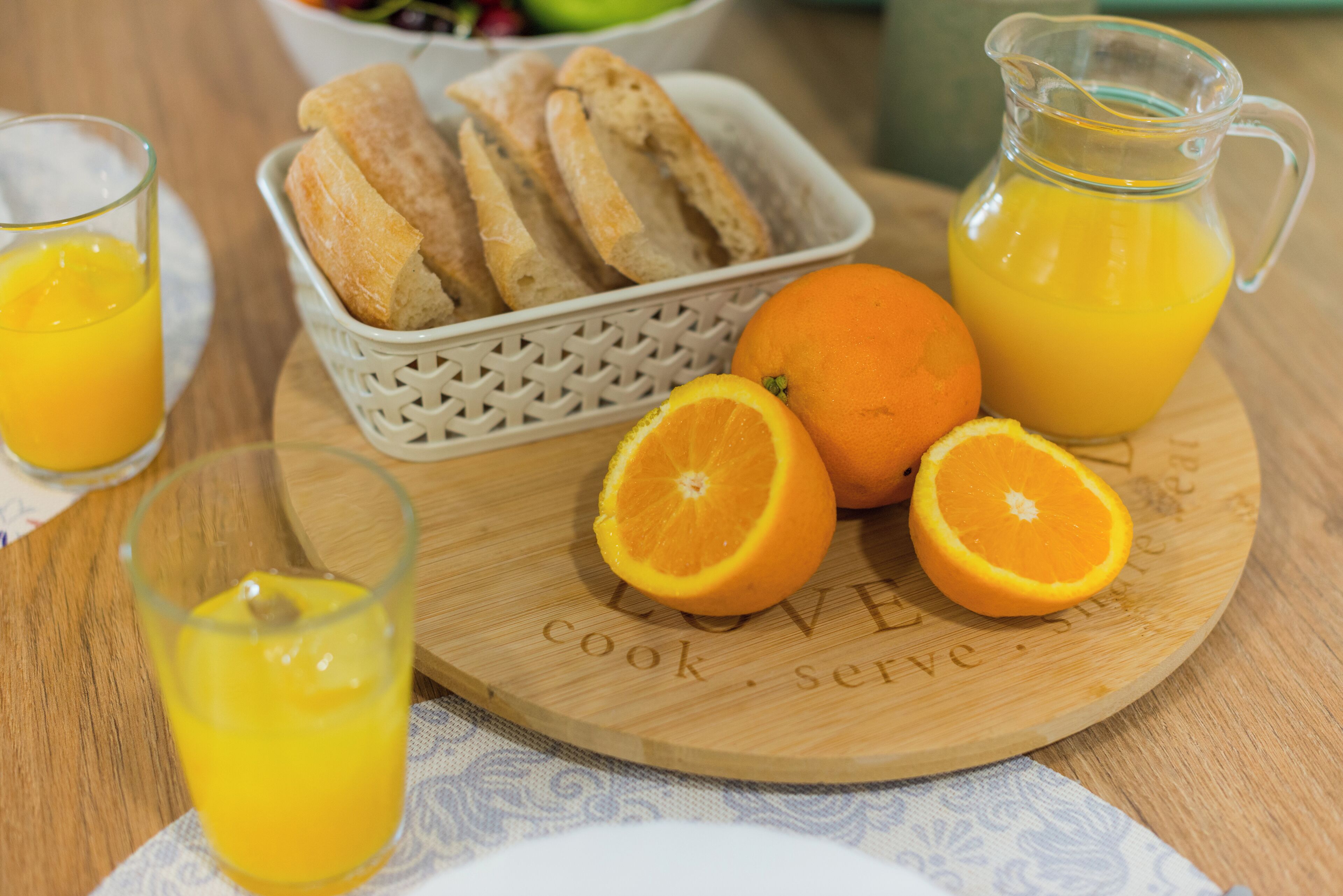 A wooden cutting board with bread and oranges, and a pitcher of orange juice.