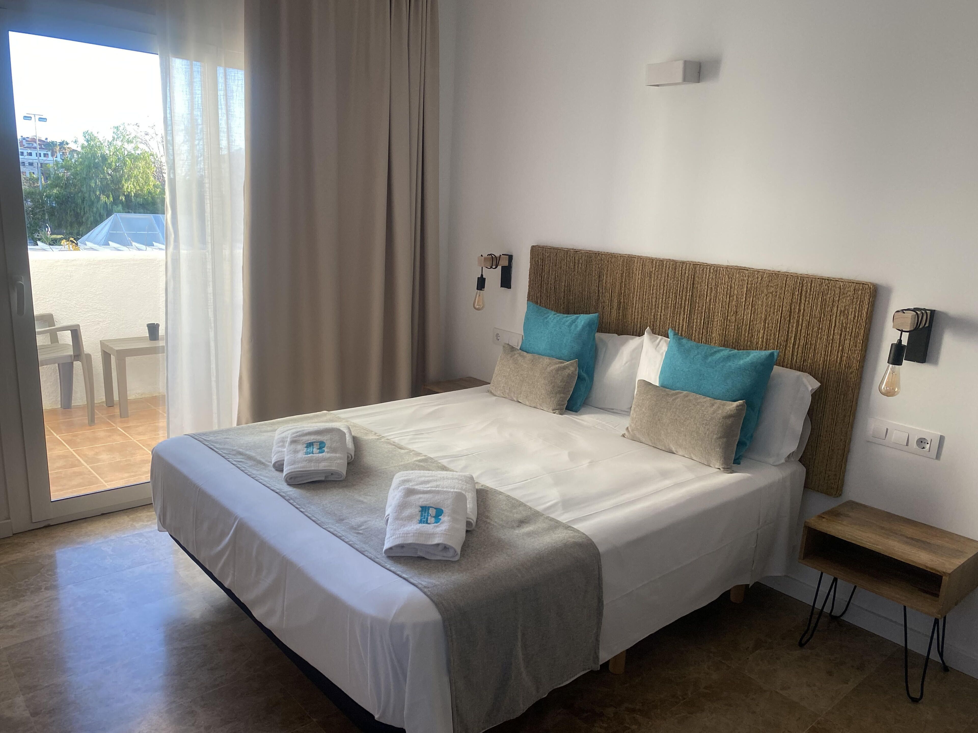 A hotel room with a large bed, two bedside tables, a view of the outdoors, and a window with curtains.