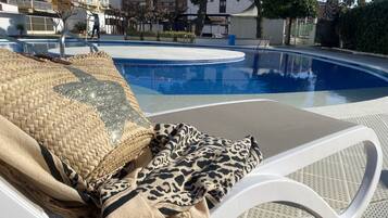 Zona de piscina con sillones de descanso, un cojín tejido y una manta de estampado de leopardo.