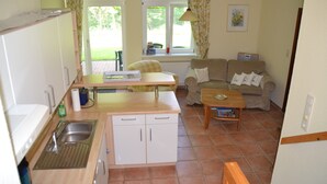 A compact kitchen with a sink, countertop, and cabinets. There is a dining area with a table and chairs, and a living room with a sofa and a coffee table. - Idyllically situated vacation apartment 10 min. to the natural beach (Barkelsby)
