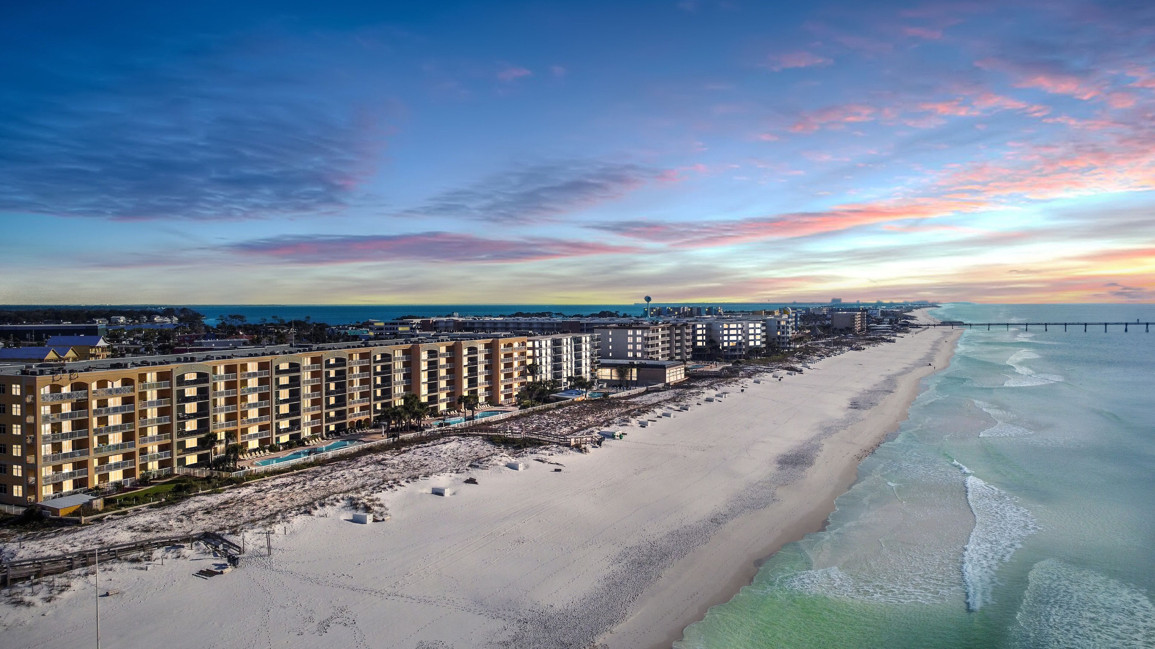 A beachfront hotel with multiple balconies, a pool area, and a view of the ocean.