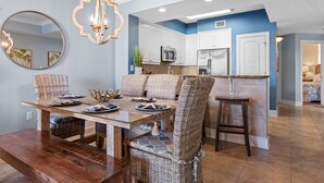 A dining area with a wooden table and wicker chairs, a kitchen with white cabinets, and a blue accent wall. - Azure 422 ~ Ocean Views ~ 2 Sets of Free Beach Service (Fort Walton Beach)