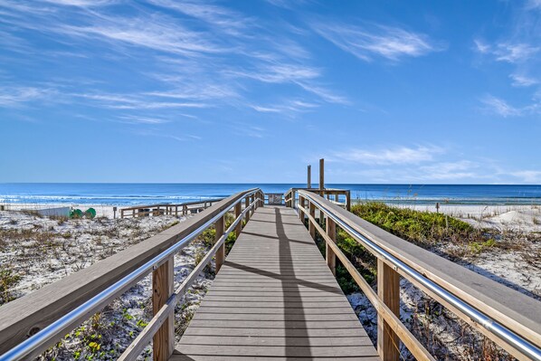 A wooden boardwalk leading to a beach with a clear blue sky.