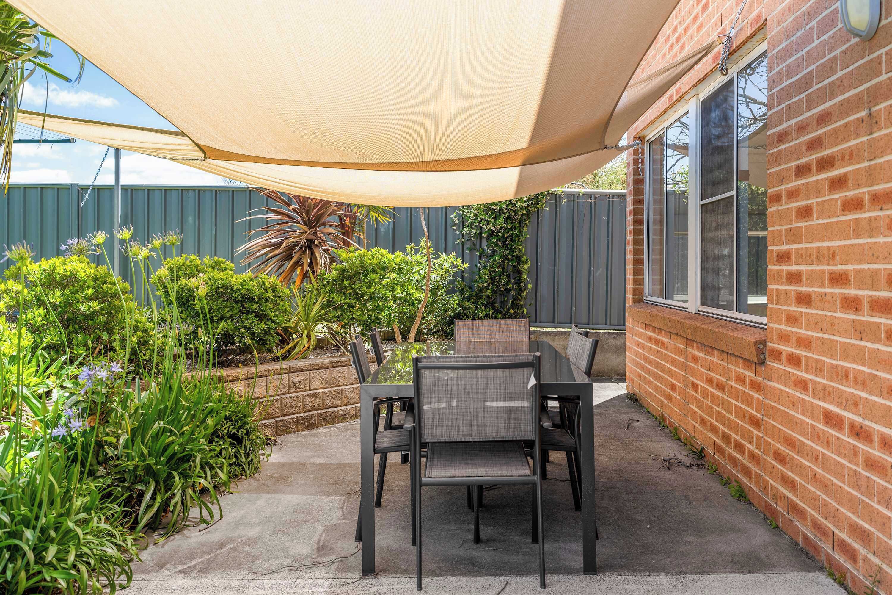 A patio with a table and chairs, a shade sail, and a brick wall.