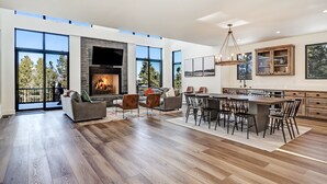 A spacious living area with a fireplace, large windows, and a modern kitchen. - Pet Friendly | Minutes to Lift | Hot Tub | Blue Mountain Escape (Angel Fire)