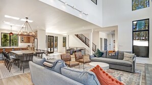 A spacious living area with a large sofa, a dining table, and a staircase leading to an upper level. - Pet Friendly | Minutes to Lift | Hot Tub | Blue Mountain Escape (Angel Fire)