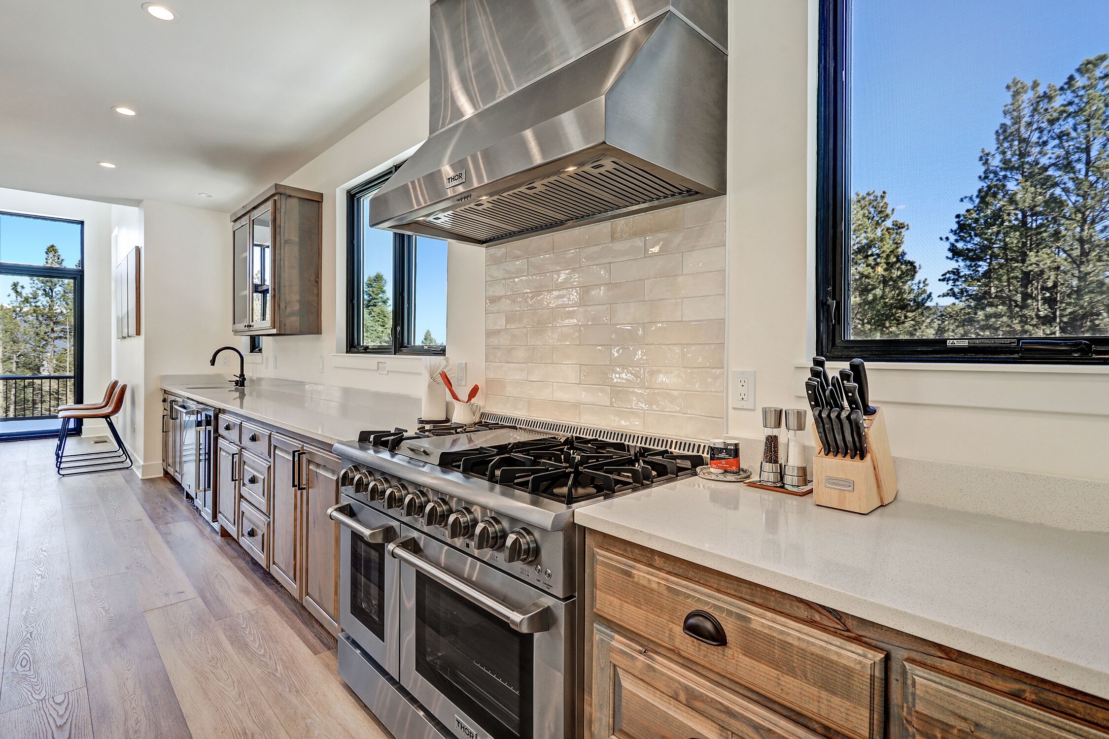 A modern kitchen with stainless steel appliances, a large window, and a view of trees.