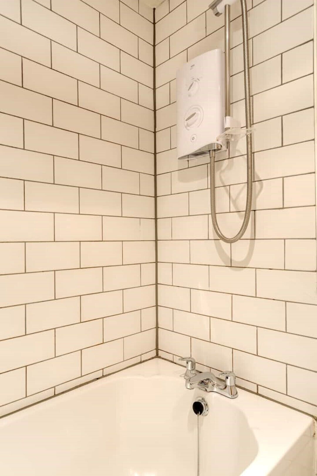 A corner shower with a white tiled wall and a bathtub.
