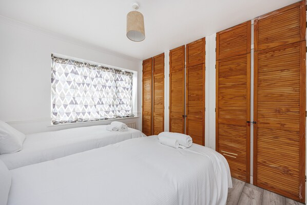 Two single beds with white linens, a large window, and a wooden wardrobe offer ample space for rest and relaxation.