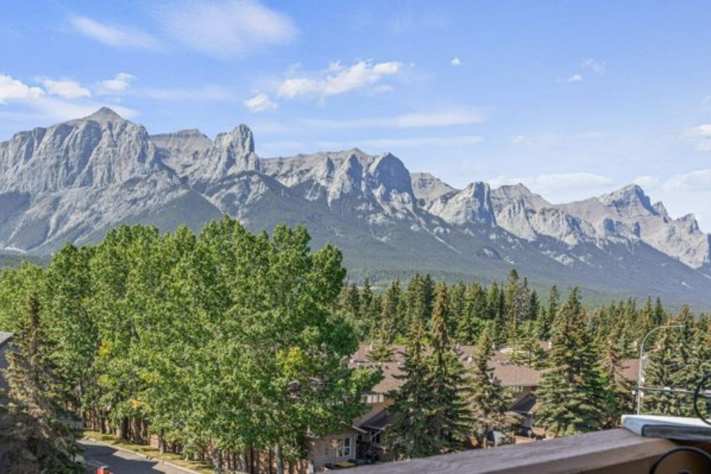 A residential area with houses surrounded by dense green trees and a mountain range in the background.