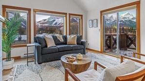 A modern living room with a dark blue sofa, a round wooden coffee table, and a large window offering a mountain view.