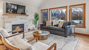 A cozy living room with a fireplace, a gray sofa, and large windows with a mountain view.